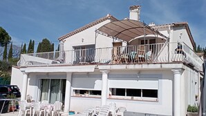 Una casa de dos pisos con piscina, un patio cubierto con sillones de descanso y un balcón grande.