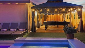 A pool area with lounge chairs, a pool table, and a covered seating area with string lights. - Grand North LV Escape w/ Pool, Spa, Arcade & Games! (North Las Vegas)