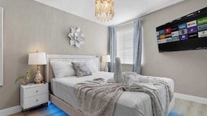 A modern bedroom with a bed, nightstands, a wall-mounted TV, and a decorative wall piece. - Grand North LV Escape w/ Pool, Spa, Arcade & Games! (North Las Vegas)