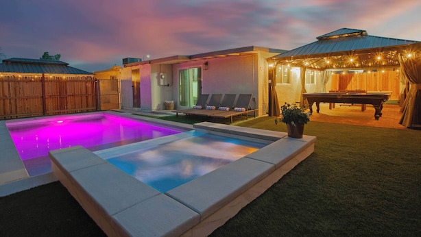 A swimming pool with a colorful light feature, a covered seating area with a table, and a fenced yard. - Grand North LV Escape w/ Pool, Spa, Arcade & Games! (North Las Vegas)