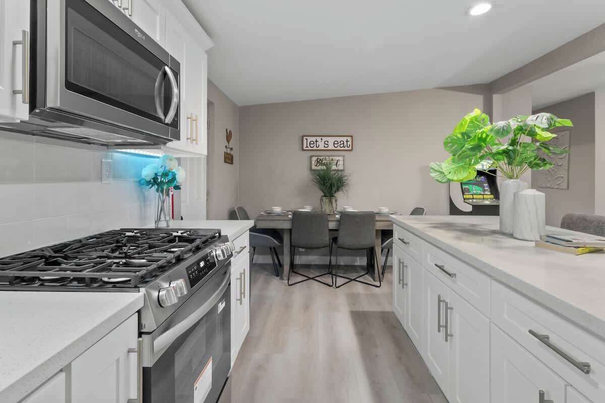 A modern kitchen with a gas stove, oven, microwave, and a dining area with chairs and a table.