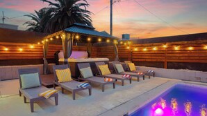 Un espace extérieur avec une piscine, des chaises longues, un coin salon abrité et des guirlandes lumineuses.