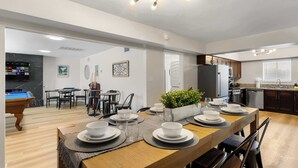 Un espace de repas moderne avec une longue table dressée pour quatre personnes, un billard et une cuisine en arrière-plan.