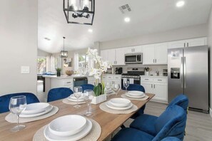 Una cocina moderna con armarios blancos, un refrigerador de acero inoxidable y un comedor con sillas azules y una mesa de madera para cuatro.