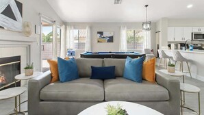 Ein modernes Wohnzimmer mit grauem Sofa, Billardtisch und Küchenzeile.