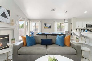 Una sala de estar moderna con un sofá gris, una mesa de billar y una zona de cocina.