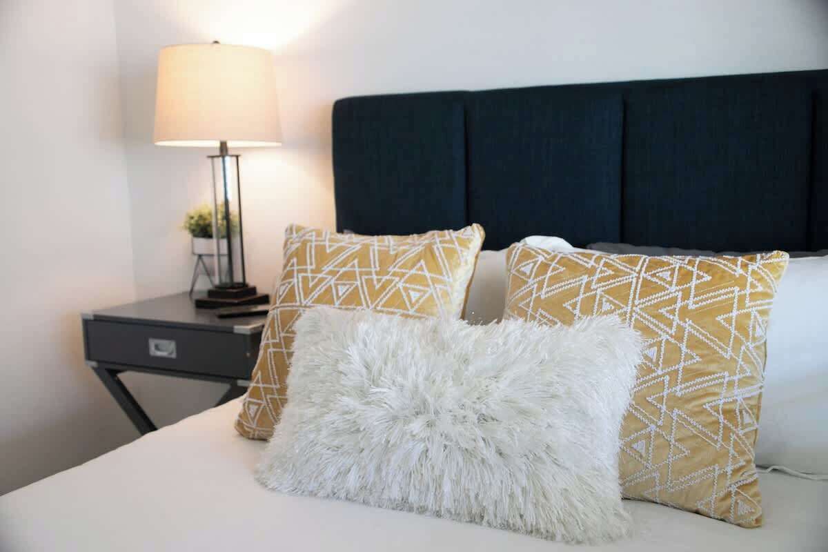 A bed with patterned pillows, a white fluffy pillow, and a dark headboard.