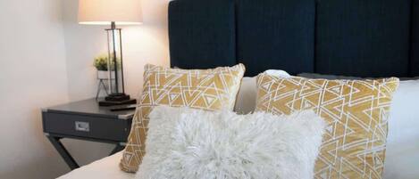 A bed with patterned pillows, a white fluffy pillow, and a dark headboard.