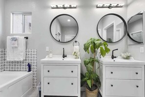 A bathroom with two sinks, a mirror, a towel rack, a potted plant, and a patterned tile backsplash. - Jackpot 6BR w/ Arcade • Vegas Fun Near the Strip (North Las Vegas)