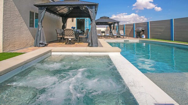 A swimming pool with a hot tub, lounge chairs, and a covered seating area.