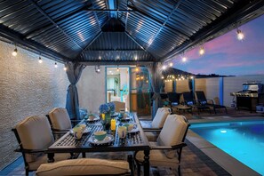 An outdoor patio with a pool, dining table, chairs, and a grill area. - Jackpot 6BR w/ Arcade • Vegas Fun Near the Strip (North Las Vegas)