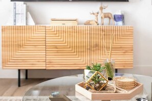 Een moderne woonkamer met een houten kast, een glazen salontafel en decoratieve objecten, waaronder een plant, een glazen vaas en een geweven dienblad.