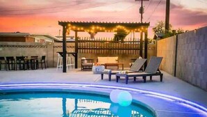 A pool area with lounge chairs, a pergola with string lights, and a view of a sunset. - Radiant Pool Retreat: 4BR NLV Getaway (North Las Vegas)