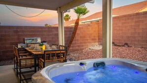Een hottub met blauwe verlichting, een barbecuegrill en een tafel met stoelen in een overdekte buitenruimte.