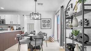 Een moderne keuken met witte kasten, een eethoek met een ronde tafel en stoelen, en een zwart wandrek met decoratieve objecten.