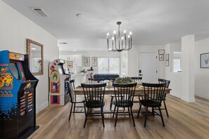 A dining area with a wooden table, black chairs, and arcade games. - Good Vibes Only – 5BR w/ Pool, Hot Tub & Game Zone (North Las Vegas)