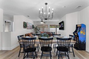 A dining area with a chandelier, a ceiling fan, and a retro arcade machine. - Good Vibes Only – 5BR w/ Pool, Hot Tub & Game Zone (North Las Vegas)