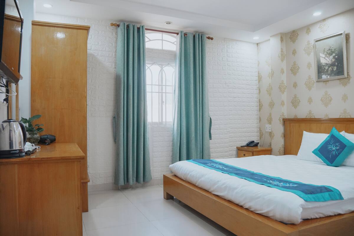 Un dormitorio con cama de madera, una mesita de noche, una ventana con cortinas y un cuadro colgado en la pared.