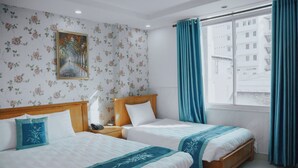 A hotel room with two beds, a wooden headboard, a nightstand, a painting on the wall, and a window with curtains. - Bohemia Hotel (Ho Chi Minh City)