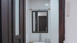 A bathroom with a white sink, dark wooden door, and a trash bin. - Bohemia Hotel (Ho Chi Minh City)