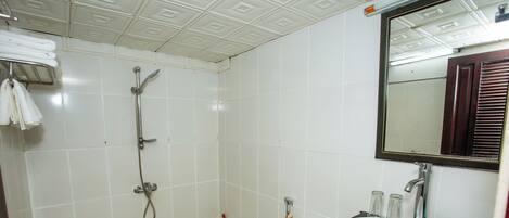 A bathroom with white tiles, a shower, a toilet, a sink, and a mirror.