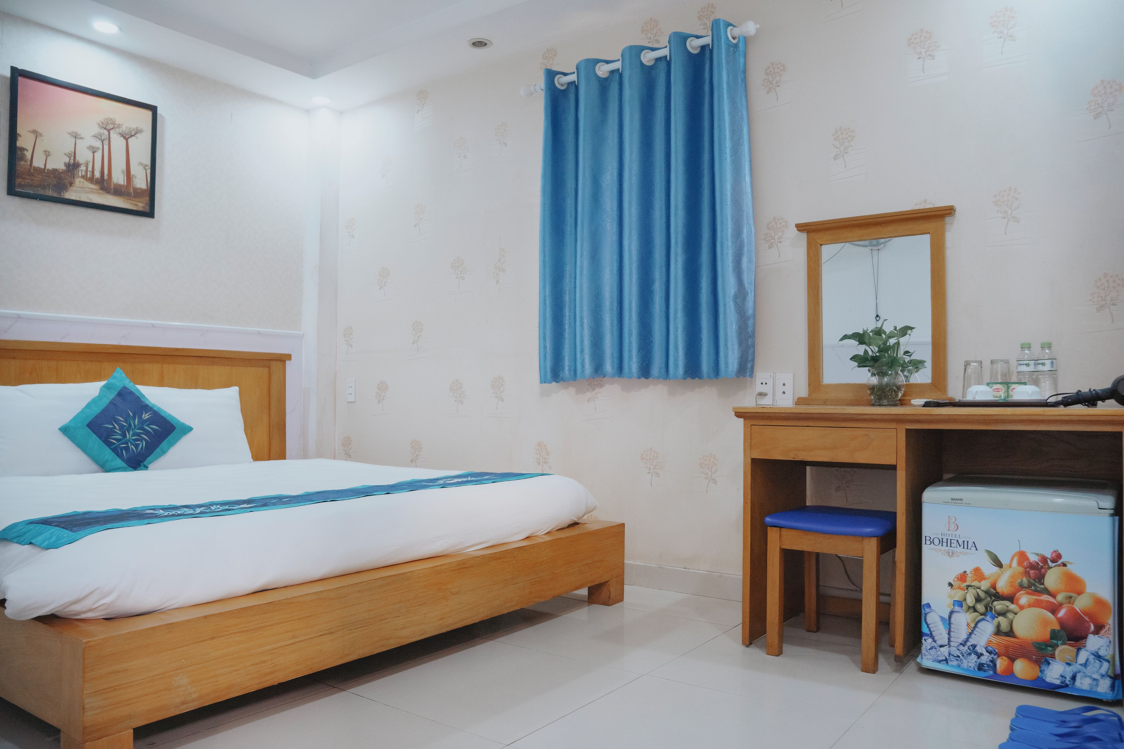 Een slaapkamer met een houten bed, een blauw gordijn, een bureau met spiegel en een koelkast.