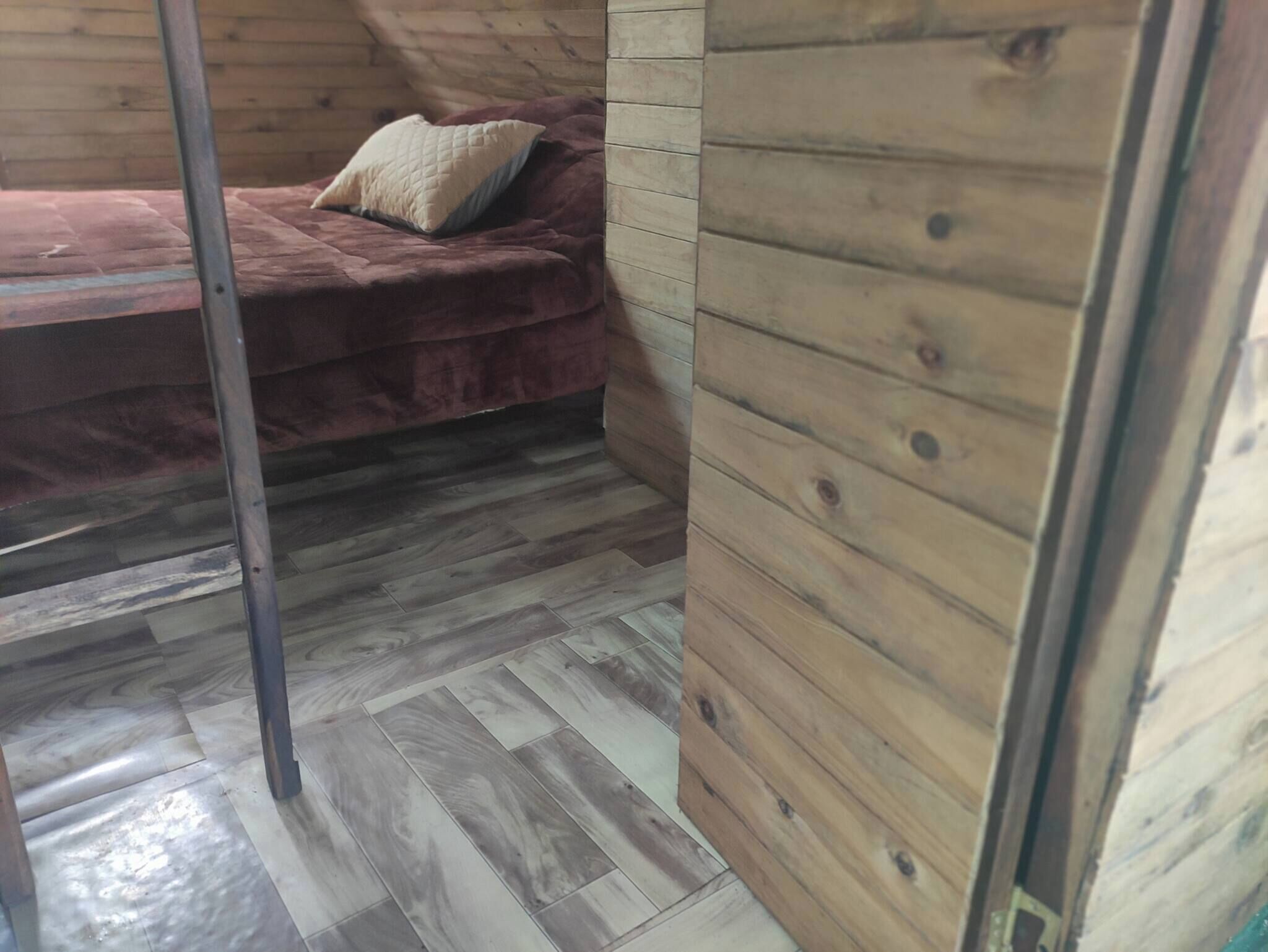 A wooden interior with a bed, a metal pole, and a wooden wall.