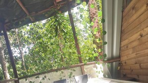 A bathtub with two empty cups, a wooden wall, and a view of greenery through a mesh window.