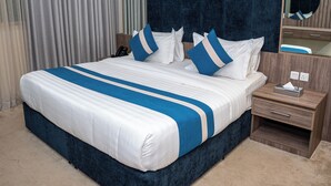 Una habitación de hotel con una cama grande, una mesita de noche con lámpara, un espejo y un atril con teléfono.
