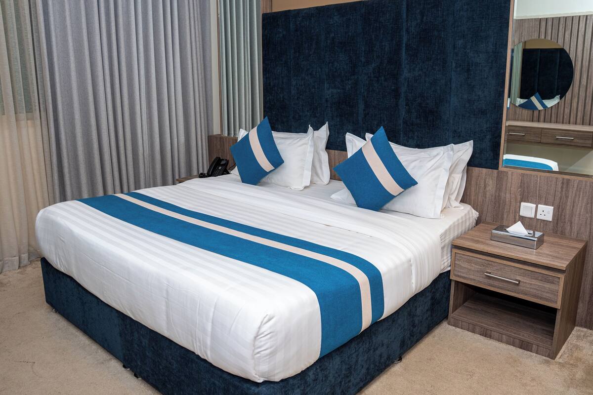 Ein Hotelzimmer mit einem großen Bett, einem Nachttisch mit Lampe, einem Spiegel und einem Beistelltischchen mit Telefon.