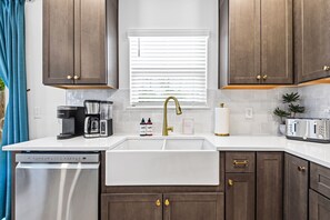 A kitchen with a dishwasher, coffee maker, toaster, and a window with blinds.