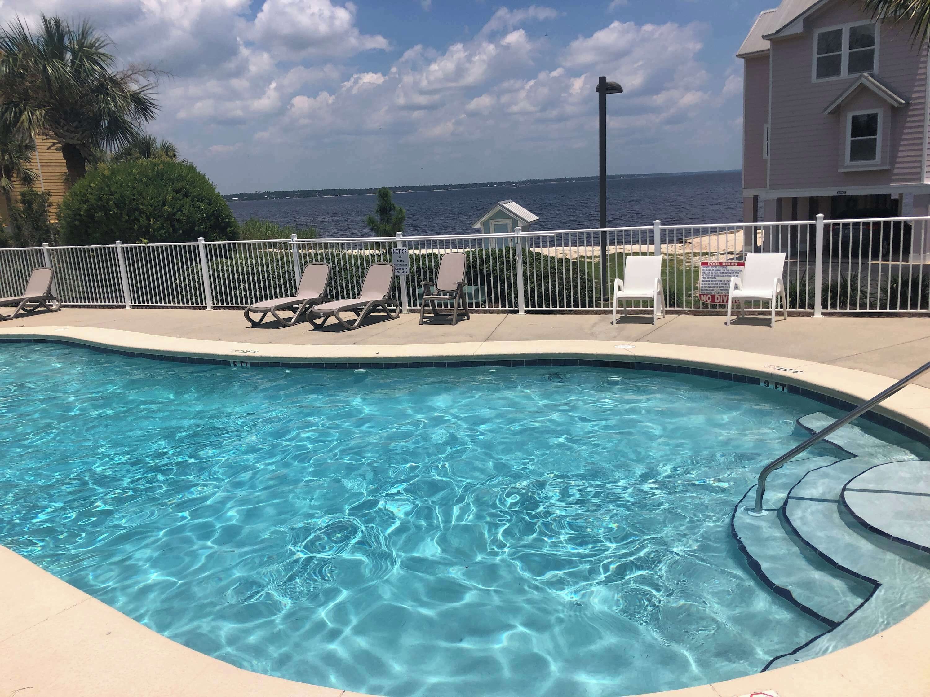 A swimming pool with clear water, surrounded by a white fence, and a view of the sea in the background.