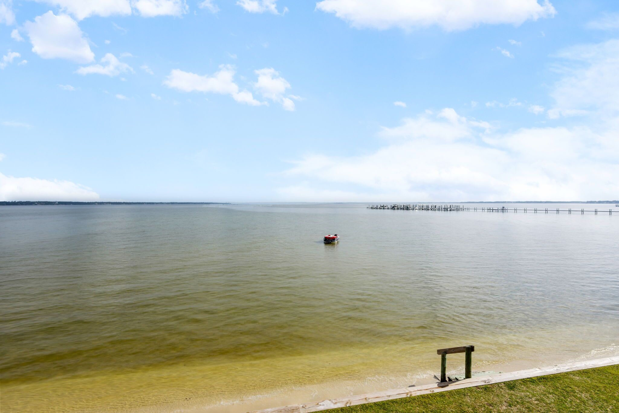 A calm body of water with a pier extending into it, a small boat, and a bench on the shore.