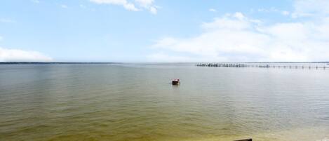 A calm body of water with a pier extending into it, a small boat, and a bench on the shore.
