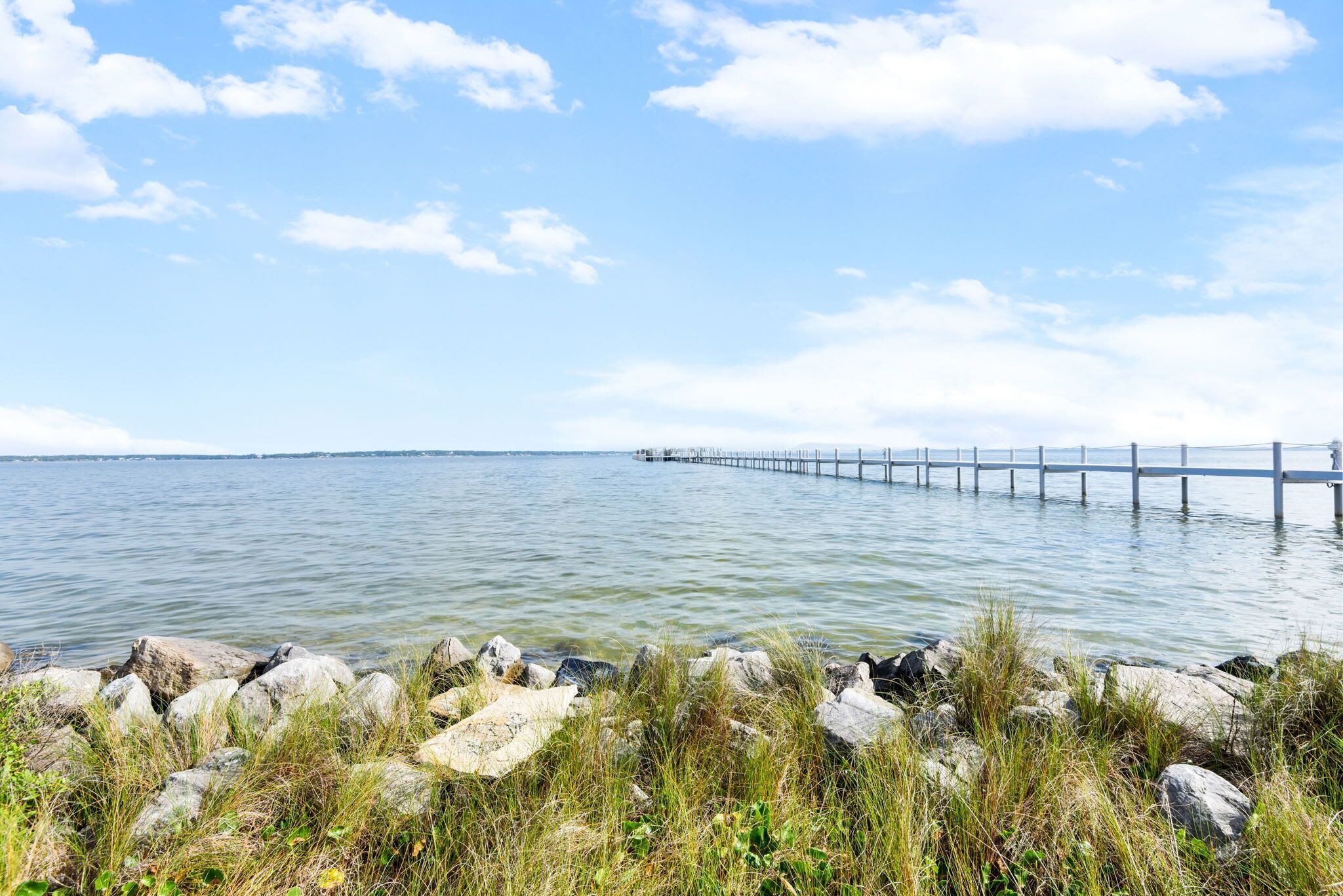 A pier extending into calm water with a rocky shoreline in the foreground.
