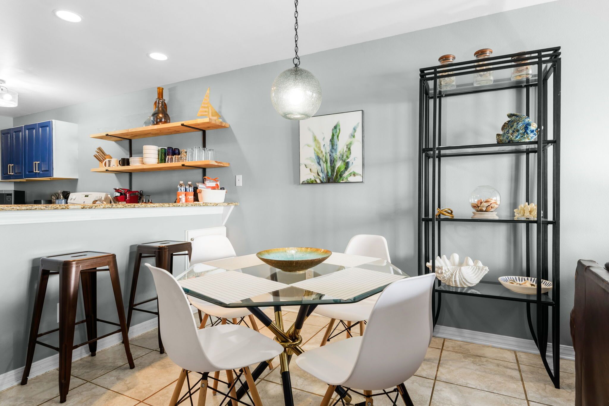 Una cocina moderna con una mesa de comedor de vidrio, sillas blancas y una estantería metálica negra.