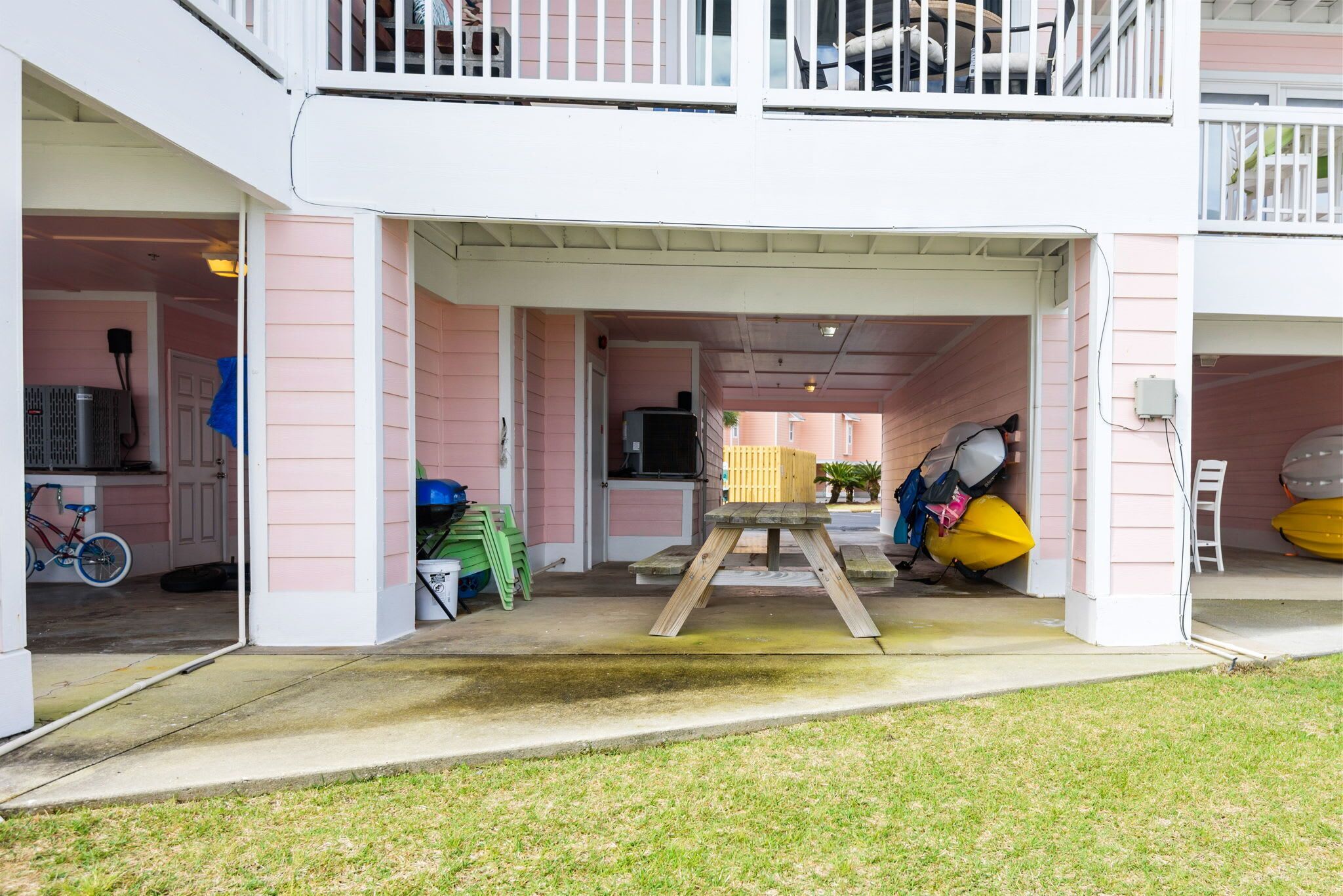 A two-story building with a covered outdoor area, a wooden table, and various items like a bicycle and kayaks.