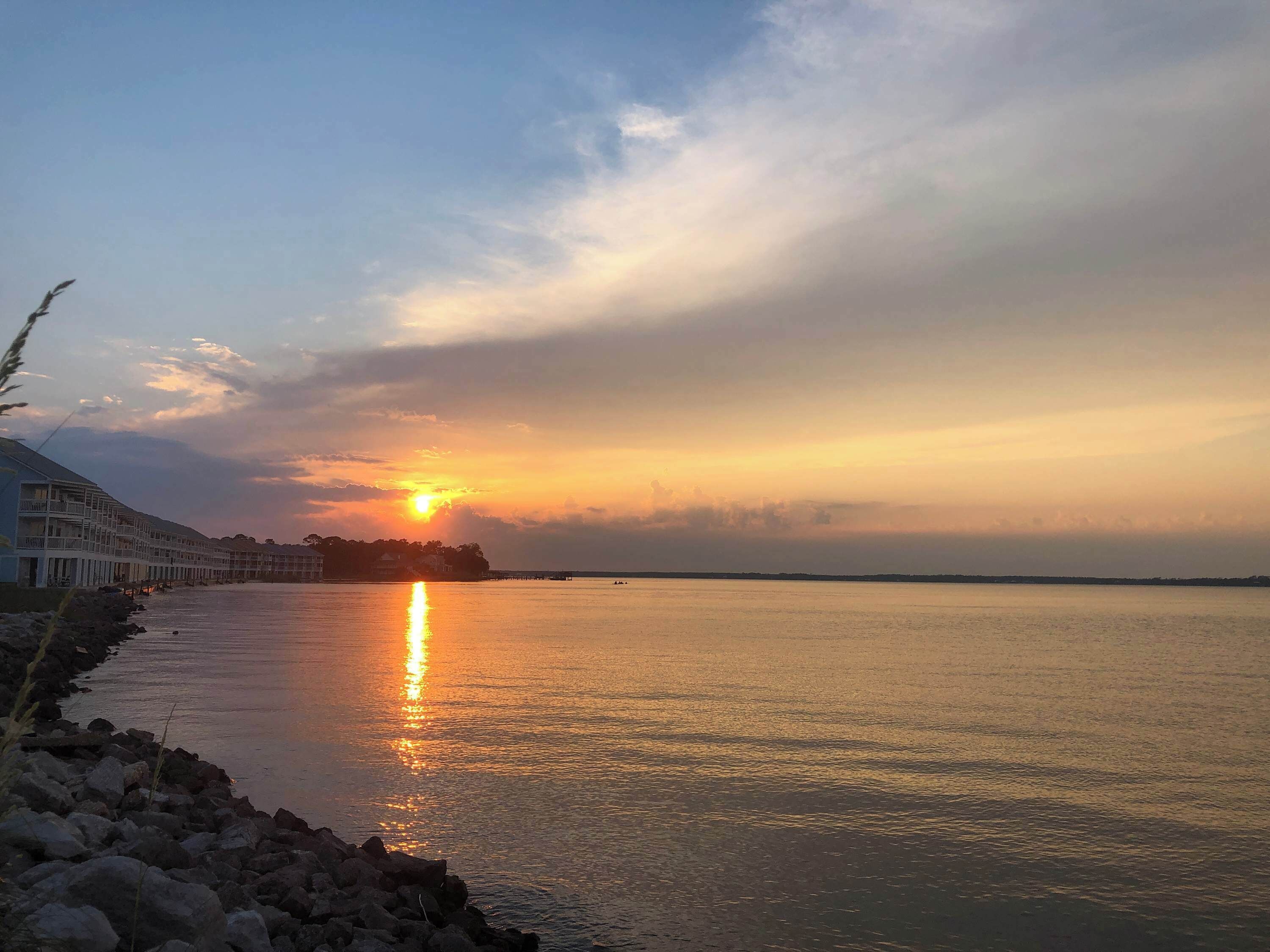 A waterfront hotel with a sunset view, calm water, and a rocky shoreline.