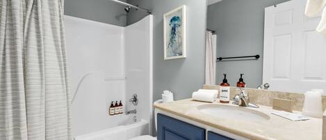 A bathroom with a shower, toilet, bathtub, and a sink with toiletries.