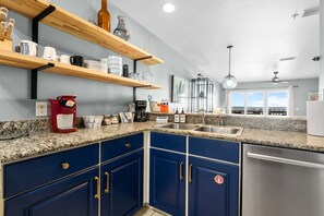 A kitchen with blue cabinets, granite countertops, and wooden shelves. - Bayfront Paradise-Steps to Sand, Pool, Kayaking (Pensacola)