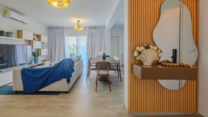 A modern living room with a sofa, dining table, and chairs, a large mirror, and a ceiling light fixture. - Tracadero Lodge PH C7 - 2 Hab Apto (Dominicus)