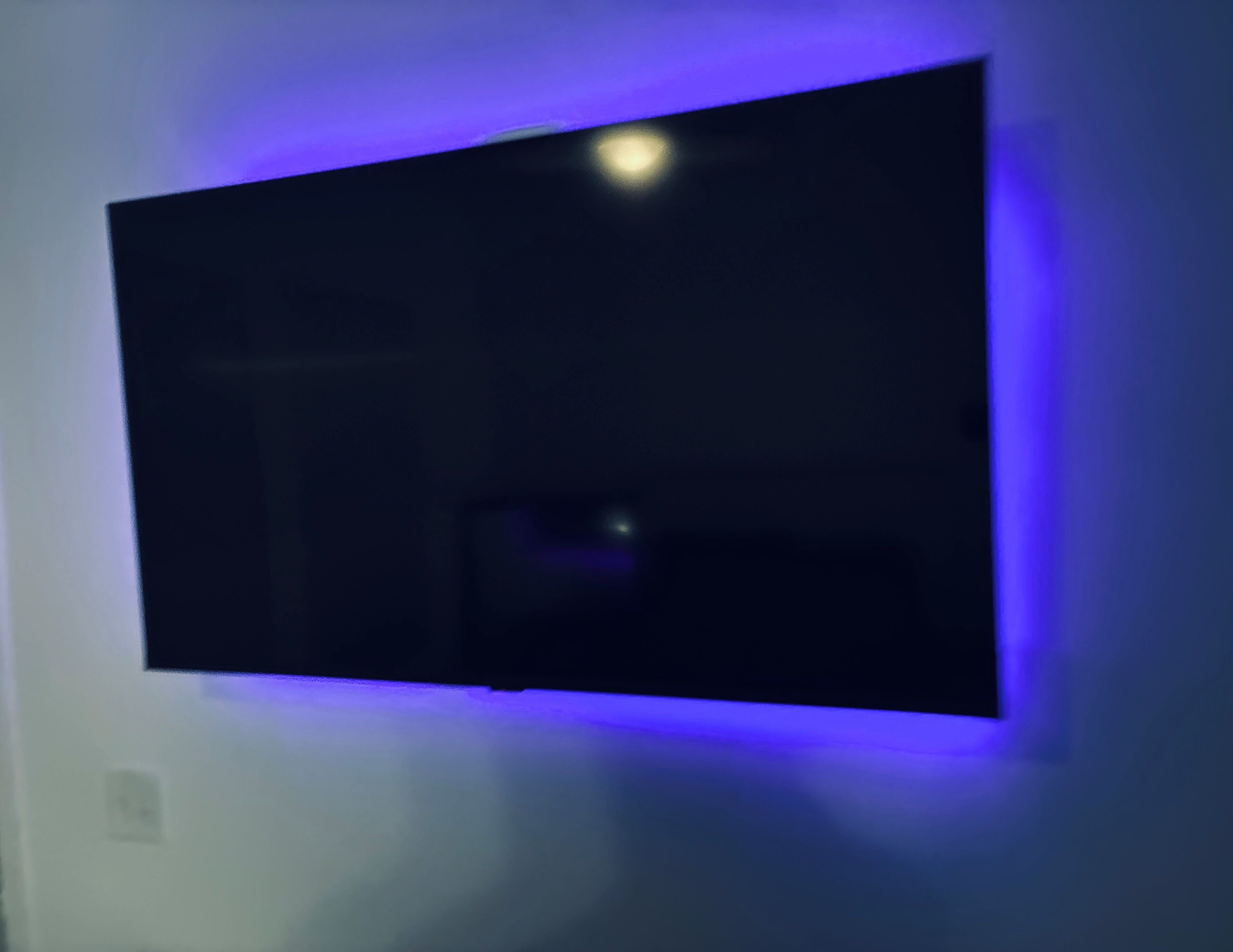 Un téléviseur à écran plat fixé au mur, éclairé d’une lumière bleue.