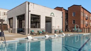 Una piscina con sillas de descanso, un edificio con un letrero y un edificio de ladrillo al fondo.
