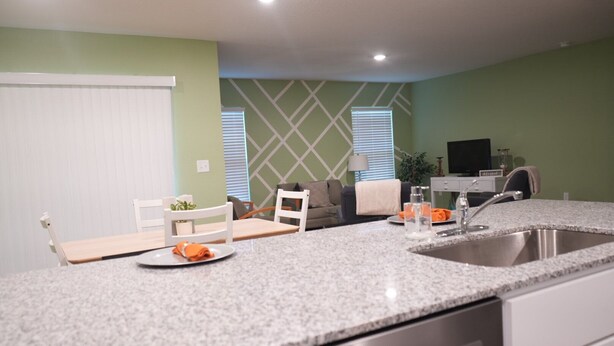 A modern kitchen with a granite countertop, stainless steel sink, and a dining area with a white table and chairs. - Unwind in this serene thoughtfully designed home nestled in a quiet neighborhood (Poinciana)