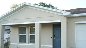 A single-story house with a front porch, a blue front door, and a garage door. - Unwind in this serene thoughtfully designed home nestled in a quiet neighborhood (Poinciana)