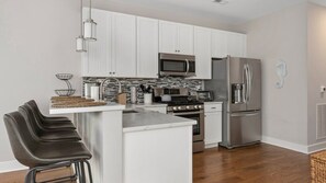 A modern kitchen with white cabinets, stainless steel appliances, and a central island with bar stools. - Residence 101S at The Sandcastle Condominiums (Wildwood Crest)