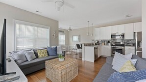 A modern kitchen with white cabinets, stainless steel appliances, and a dining area with a small island. - Residence 101S at The Sandcastle Condominiums (Wildwood Crest)