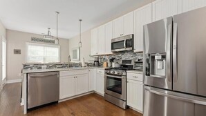 A modern kitchen with stainless steel appliances, white cabinetry, and a wooden floor. - Residence 101S at The Sandcastle Condominiums (Wildwood Crest)