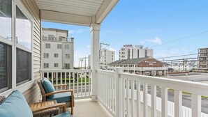 A balcony with wicker furniture, a view of a street, and buildings in the background. - Residence 101S at The Sandcastle Condominiums (Wildwood Crest)
