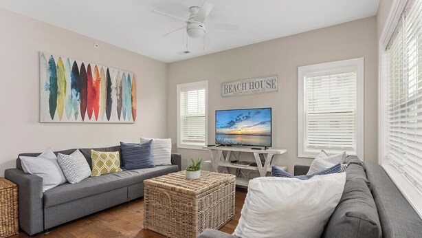 A living room with a gray sofa, a television, a wicker coffee table, and a wall-mounted artwork. - Residence 101S at The Sandcastle Condominiums (Wildwood Crest)